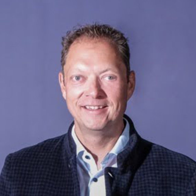 Porträt eines lächelnden Mannes in Blazer vor lilafarbenem Hintergrund